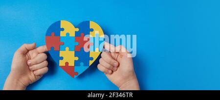 Autistic boy hands holding jigsaw puzzle heart shape. Autism spectrum disorder family support concept. World Autism Awareness Day Stock Photo