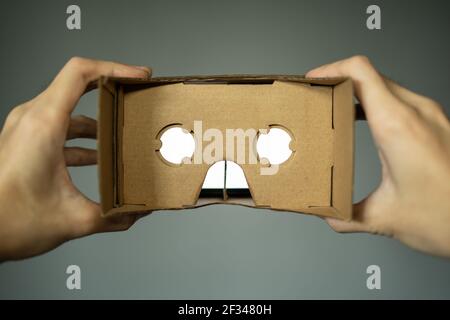 Hand holding VR headset made of cardboard. First person point of view. Stock Photo