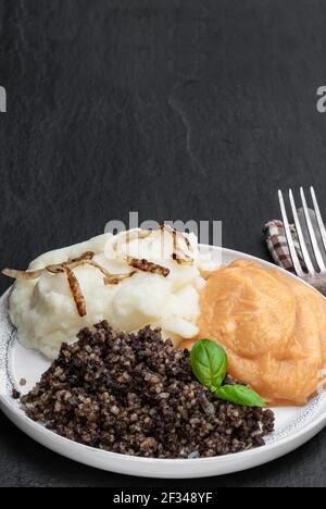Traditional  Scottish haggis with neeps and tatties on black stone background Stock Photo
