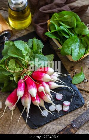 Summer salad ingredients, organic vegetables and olive oil. Raw fresh juicy radish on a rustic table. Stock Photo