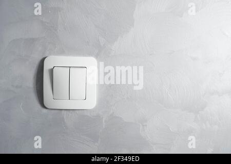 Light switch, a plastic mechanical switch of white color installed on a light gray wall. Stock Photo
