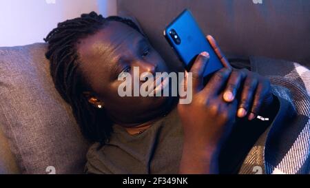 Bored black man using smartphone while resting on the couch. High quality photo Stock Photo