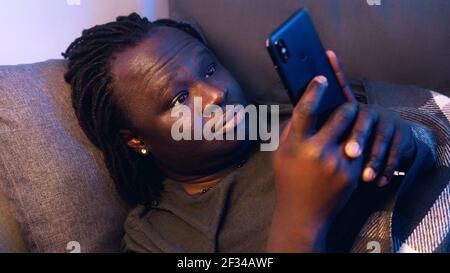 Bored black man using smartphone while resting on the couch. High quality photo Stock Photo