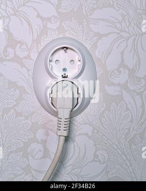white plastic wall socket on wallpaper with one plug Stock Photo