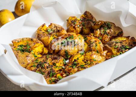 Baked smashed potatoes with herbs in oven dish. Stock Photo