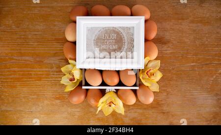 Eggs from the farm on the table surround a wooden box with a message 'Enjoy every moment'. Stock Photo