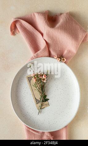 Romantic, wedding or spring table setting. Empty plate with card and little pink flowers, light concrete background. Selective focus. Stock Photo