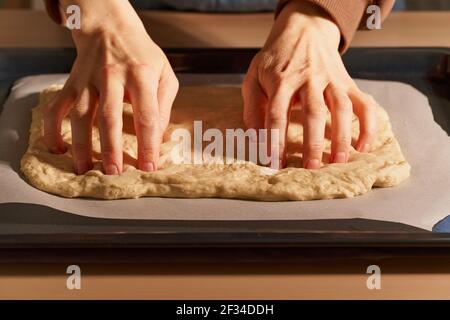 Woman preparing focaccia. Women's hands crumpling raw dough on metal tray, pressing fingers Stock Photo