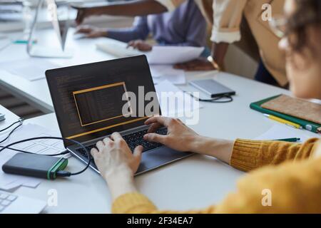 Close up of young man writing code while using laptop in office with team of software developers, copy space Stock Photo