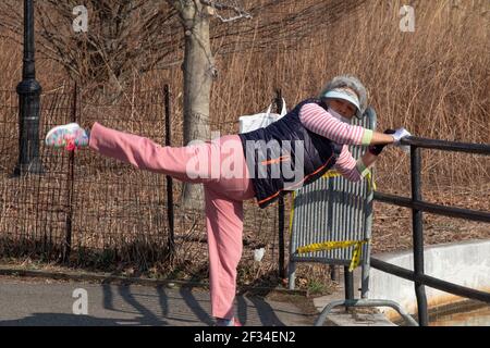 A flexible Asian American woman stretches near the lake in Kissena Park, Flushing, Queens, New York City. Stock Photo