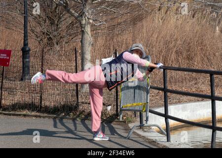 A flexible Asian American woman stretches near the lake in Kissena Park, Flushing, Queens, New York City. Stock Photo