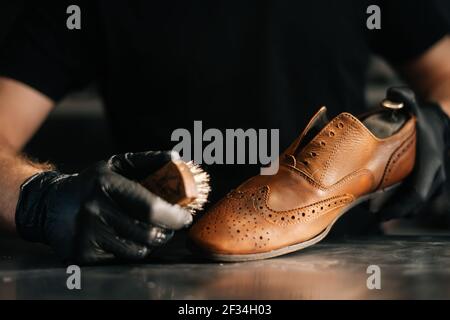 Close-up front view of unrecognizable shoemaker cleaning with brush old light brown leather shoes. Stock Photo