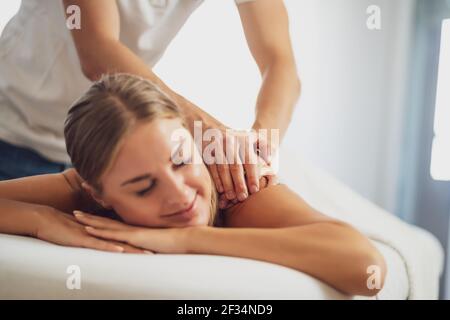 Professional masseur doing therapeutic massage. Woman enjoying massage in her home. Young woman getting relaxing body massage. Stock Photo