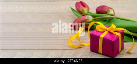 A gift and tulips on a wooden background. Spring flowers and a gift box. Red tulips and red packaging. Stock Photo