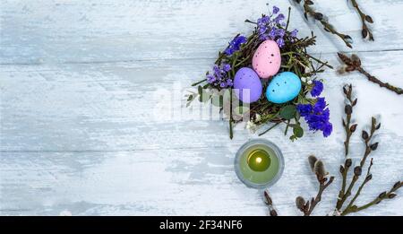 A nest with Easter eggs. Willow branches on a gray-blue background. Three Easter eggs in a nest and a candle. Stock Photo