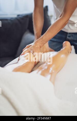 Professional masseur doing therapeutic massage. Woman enjoying massage in her home. Young woman getting relaxing body massage. Stock Photo