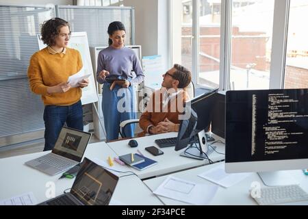 Portrait of two young people talking to male manager while discussing software development project in modern office, copy space Stock Photo