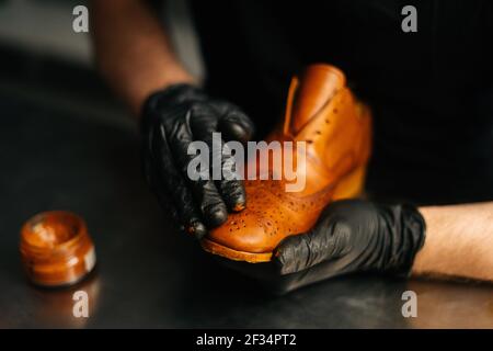 Close-up hands of shoemaker in black gloves rubbing paint on toe cup of light brown leather shoes Stock Photo