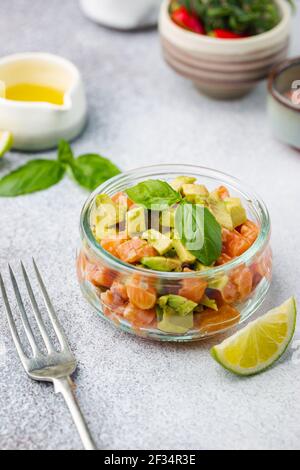 Delicious avocado and raw salmon salad, tartare, served glass jar with lime, light background Stock Photo