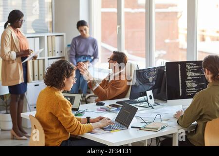 Diverse team of young software programmers using computers and writing code while collaborating on project in IT development studio, copy space Stock Photo