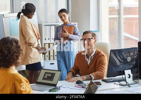 Portrait of smiling team leader talking to colleagues while collaborating on project in modern IT development studio Stock Photo