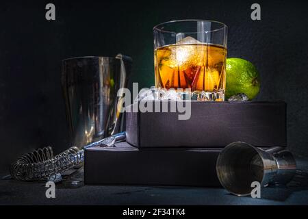 Whiskey or cognac in glass, with lime, ice cubes ans barmen utensils, dark background with on stand pedestal copy space Stock Photo