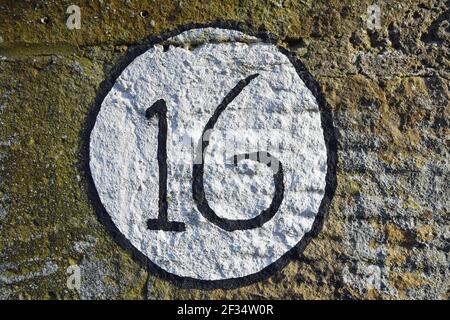 Isolated painted number 16 circular sign on stone wall Stock Photo