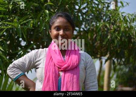 Close up of Indian Bengali teenage girl wearing white cotton salwar with pink dhupatta standing in front of a mango tree, selective focusing Stock Photo