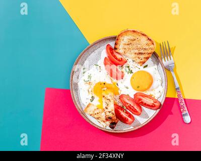 Two fried eggs with toast and vegetables on colorful background. Breakfast concept. Healthy vegetarian food. Close up, copy space Stock Photo