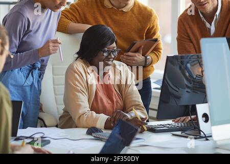 Cropped shot of diverse IT development team collaborating on project with smiling African-American woman using computer in software production studio Stock Photo