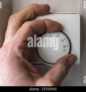 mans hand operating a central heating thermostat on the wall of a home Stock Photo