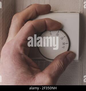 mans hand turning up the central heating temperature on a thermostat fixed to the the wall of his home Stock Photo