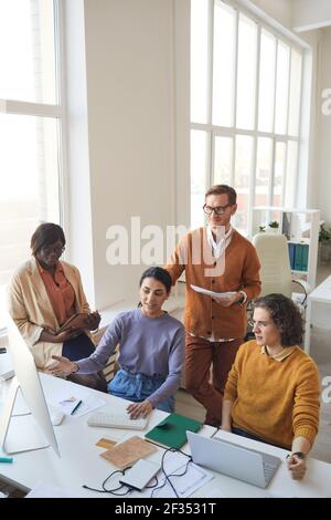 Vertical wide angle portrait of diverse IT development team discussing project while working on software production in office, copy space Stock Photo