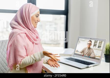 Pc screen view, islamic woman dressed in national hijab talking with male best friend, chatting using virtual modern video conference application, communicating from home, enjoy distant conversation Stock Photo