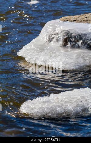 Isolated ice covered rocks beginning to thaw out on a warm sunny day along the Fox river Stock Photo