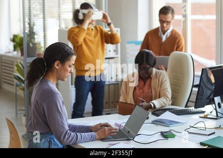 Side view portrait of female IT developer using laptop with code on screen while working in software production studio, copy space Stock Photo