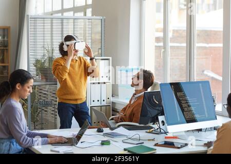Portrait of young IT developer testing VR gear while working with team at software production studio, copy space Stock Photo