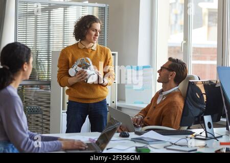 Portrait of young IT developer holding VR headset while working with team at software production studio, copy space Stock Photo