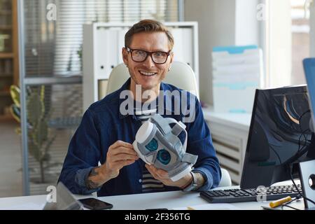 Portrait of smiling IT developer holding VR headset and looking at camera while working on augmenter reality applications, copy space Stock Photo