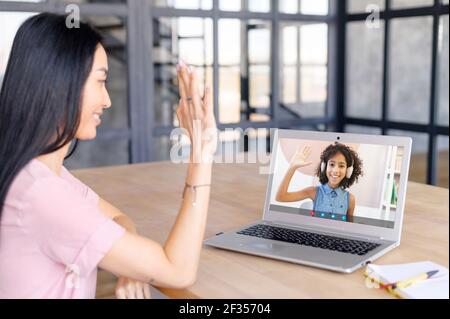 Woman teacher has video lesson, greets school-age African girl in headset, new education system, explaining, enjoying studying online or communicating with school professor via video call at home Stock Photo