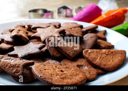 On a wooden table there is a white plate on which gingerbread cookies and icing next to them Stock Photo