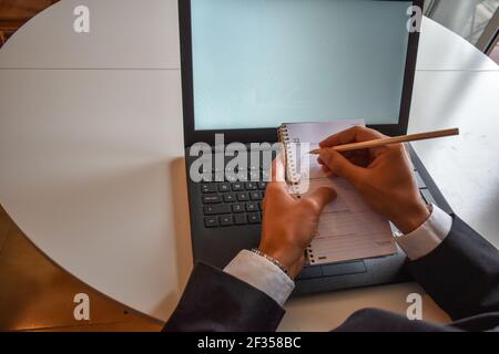 An overhead shot of a businessman writing notes in his planner and working on his laptop Stock Photo