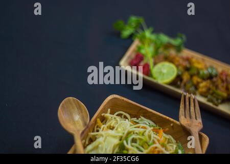 chilli chicken and noodles served on wooden plates with spoon and fork. delicious chinese food for copy space background. shallow depth of field.adver Stock Photo