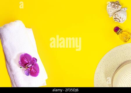 Layout is summer, beach. White terry towel with purple orchid, straw hat, bottle of perfume, seashells on yellow background. Travel and tourism. Copy Stock Photo