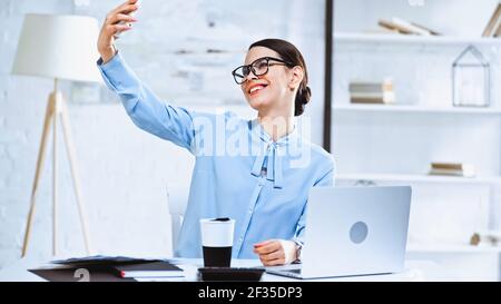 cheerful businesswoman taking selfie on smartphone in office Stock Photo