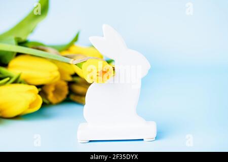 White ceramic Easter bunny, yellow daffodils and tulips on a blue background Stock Photo