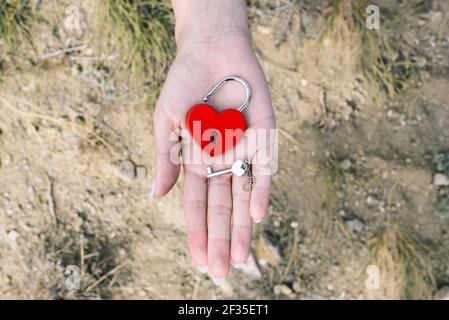 Lock and key in hand. Red metal lock in the form of a heart. Lock of love and key in the shape of a heart on a female palm. Stock Photo