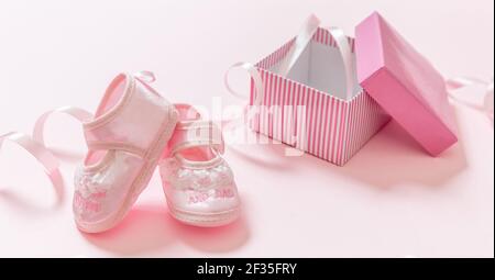 Baby pink shoes on pink color background. It’s a girl newborn announcement template. Infant soft female footwear out of an opened gift box. Baby showe Stock Photo