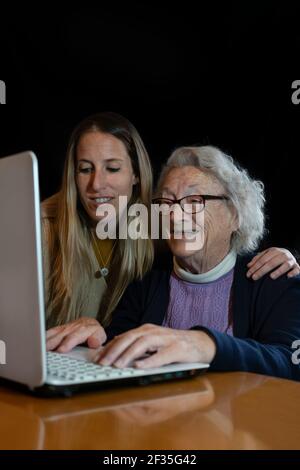Happy senior 80s woman with granddaughter using computer.Young female help or teach to surf internet grandparent.Family having fun together watching v Stock Photo