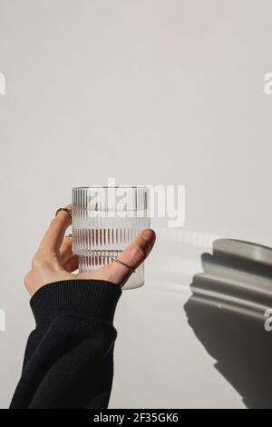 Woman's hand holds a glass of clean water over the white wall Stock Photo